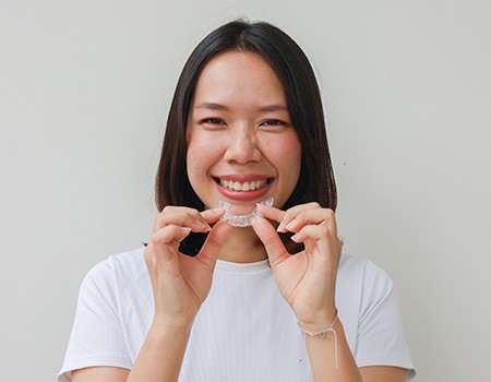 Woman smiling while holding Invisalign aligner