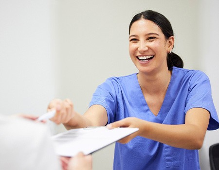 Dental assistant smiling while handing patient form