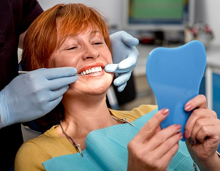 An older woman admiring her new dentures with a hand mirror