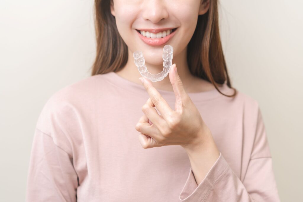 Nose-to-chest view of woman in pink sweater holding Invisalign